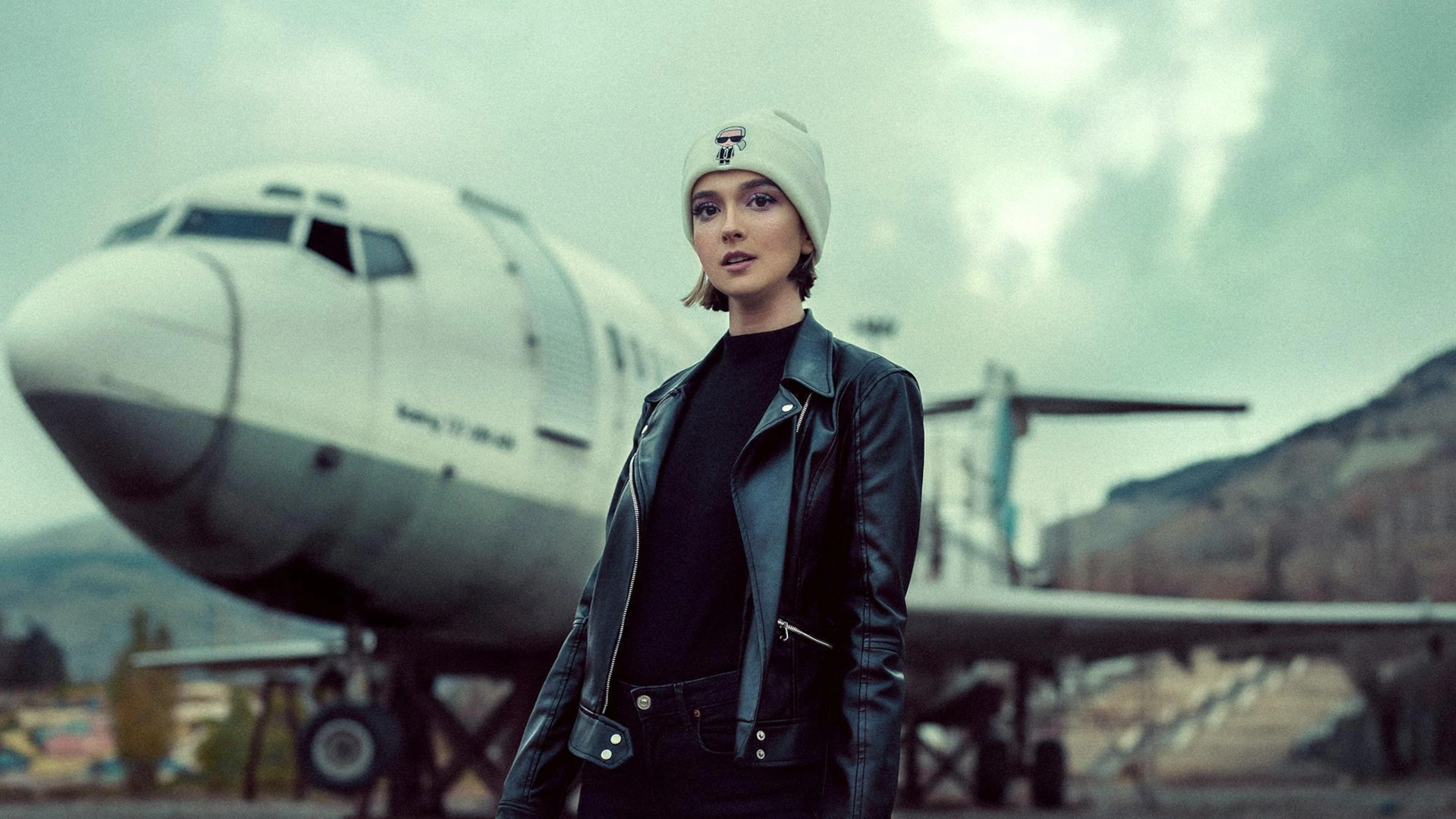 Woman in a leather jacket standing on an airport runway in front of an airplane